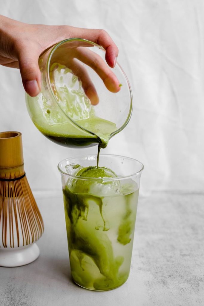 Ajout de matcha fraîchement préparé dans un verre rempli de glace pour un matcha bubble tea glacé et rafraîchissant.