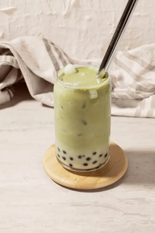 Versement d’une préparation de matcha dans un verre de bubble tea avec du lait et des perles de tapioca, créant un matcha bubble tea frais et crémeux.