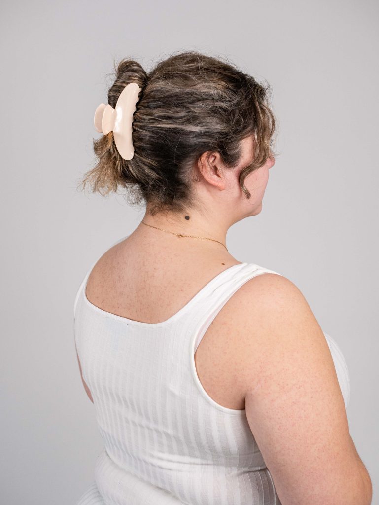 A woman is wearing a beige PixieWoo claw clip in her curly brown hair. The claw clip is holding all of her hair.