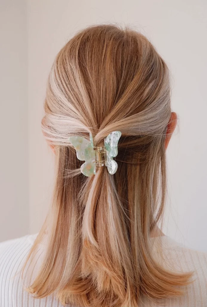 A girl is wearing a butterfly-shaped PixieWoo hair clip in her blonde hair. The clip is green, pink, and white in color. The claw clip is holding half of her hair.